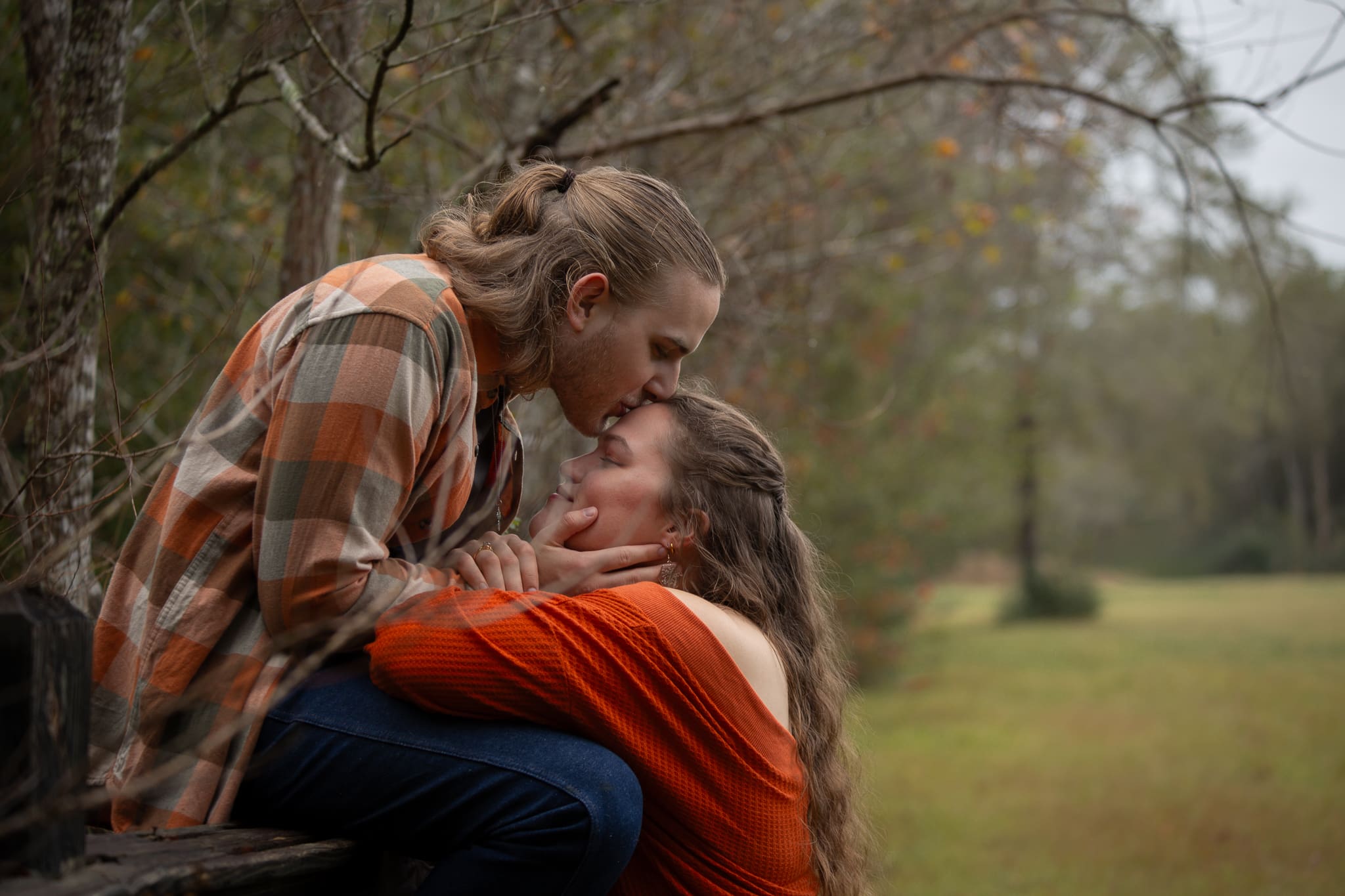 Young man sitting on a fence leans down to kiss young woman